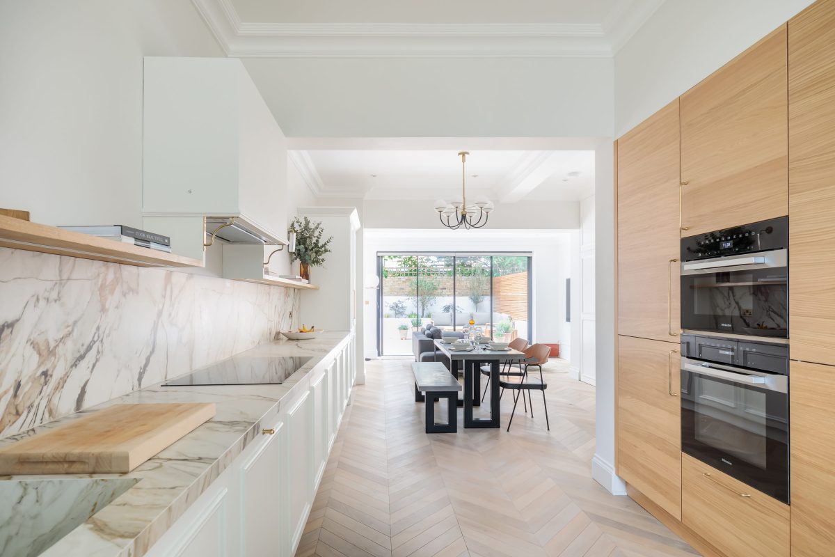 Modern kitchen featuring a combination of marble and wooden surfaces, with high-end appliances and a spacious dining area visible through large glass doors. An Arch KBB team member is present, showcasing the stylish design and open layout of the space.