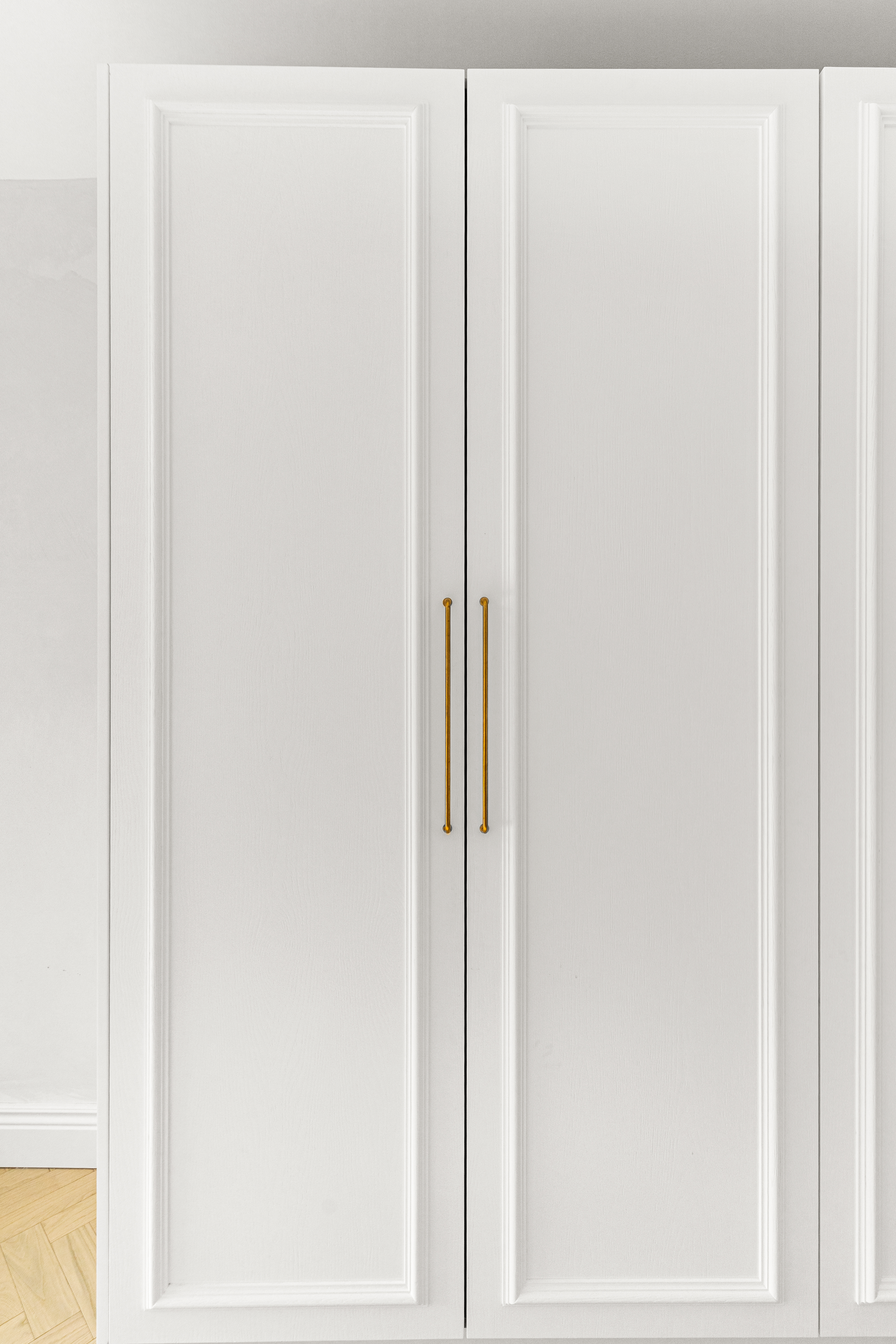 White wardrobe with gold handles, featuring a sleek design and panelled doors, situated in a modern interior setting. An Arch KBB team member is present, showcasing the stylish furniture piece.