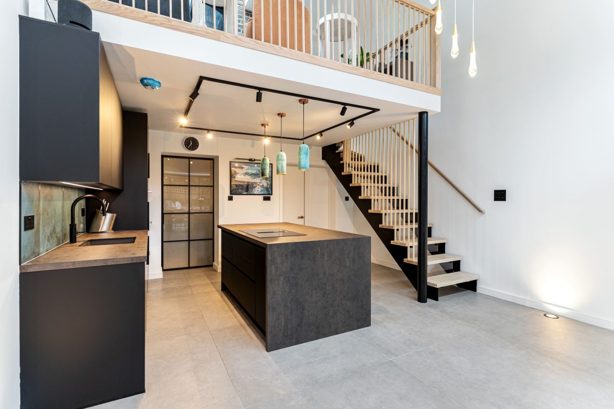 Modern kitchen design in Brent featuring a sleek island, minimalist cabinetry, and elegant pendant lighting, with a staircase leading to an upper level.