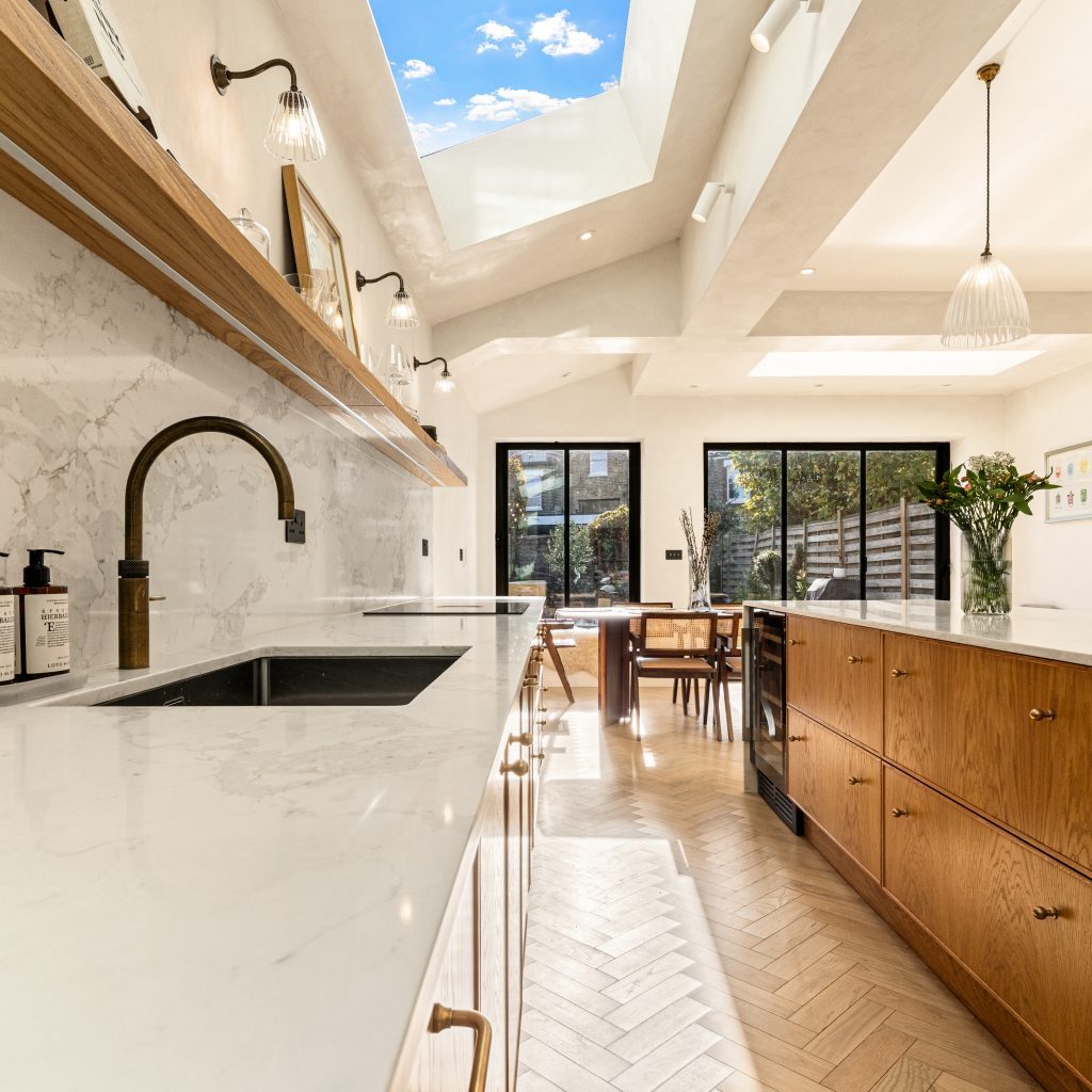 Modern Chiswick kitchen design by Arch KBB featuring white marble countertops, wooden cabinetry, and a skylight illuminating the dining area.