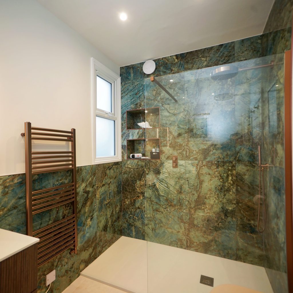 Modern bathroom design featuring a spacious walk-in shower with elegant green marble walls, glass enclosure, and a sleek towel radiator.